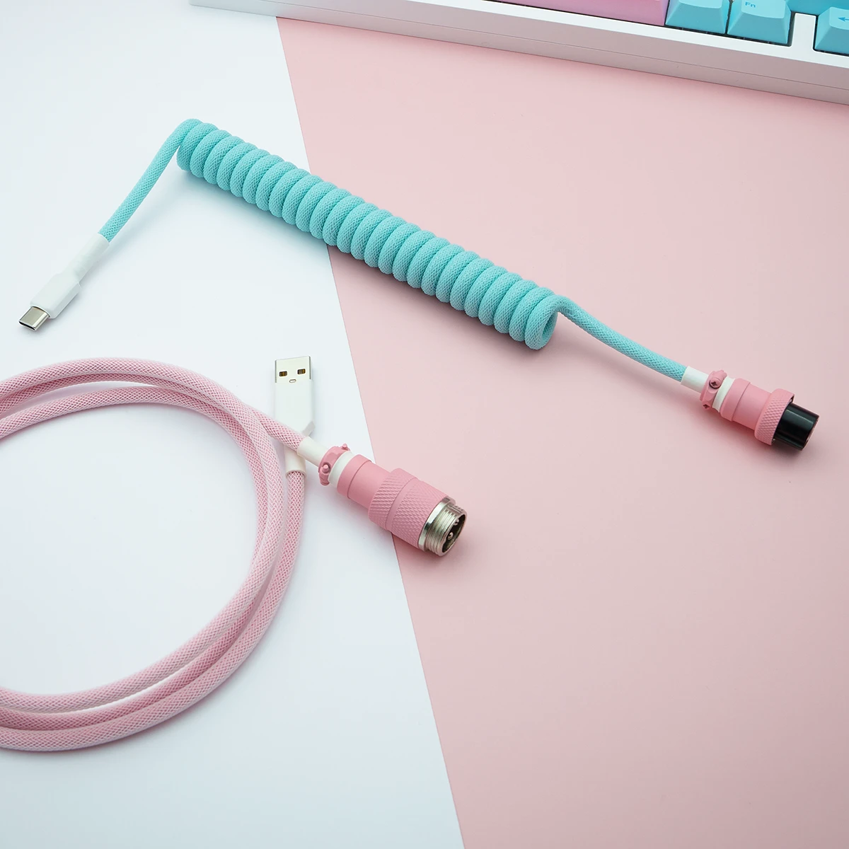 Aqua pink coiled cable usb c gx16 top view 1 Custom keyboard cable featuring a coiled design in light blue and pink, with USB-C and AVIATOR connectors, high-quality braiding, and smooth textures.