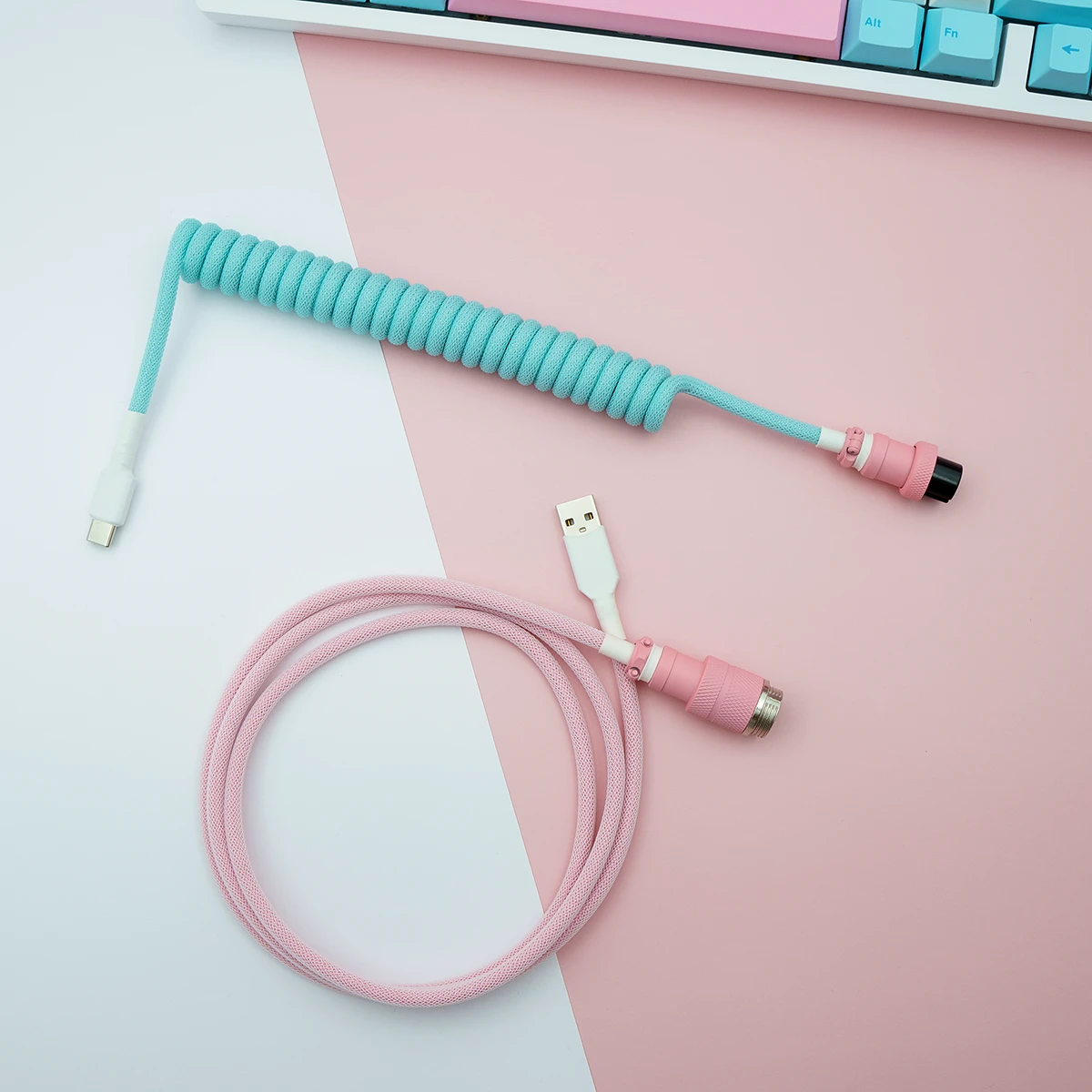 Aqua pink coiled cable usb c top view 1 Custom keyboard cable features a coiled aqua blue section and a straight pink part. It includes USB-C and aviator connectors, showcasing quality braiding.