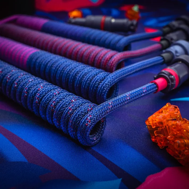 Blaues Spiralkabel USB C gewinkelt lebendig Eine Nahaufnahme des GMK Laser Keyboard Cable zeigt ein farbenfrohes geflochtenes Design mit Spulen in verschiedenen Längen und abnehmbaren USB-C- und Pilotensteckern.