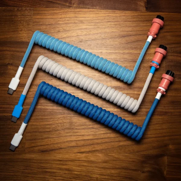 Blue gray coiled cables overhead lemo connectors 1 Three custom keyboard cables are displayed on a wooden surface, featuring coiled paracord textures. Each cable has detachable connectors—USB-C and aviator. The vibrant blue and gray colors are complemented by precision CNC metal housings and quality braiding.