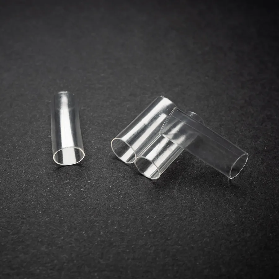 Four Clear Heatshrink (6.5mm) – (1/4) transparent plastic tubes are lying on a black surface, with three grouped together and one separated to the left.