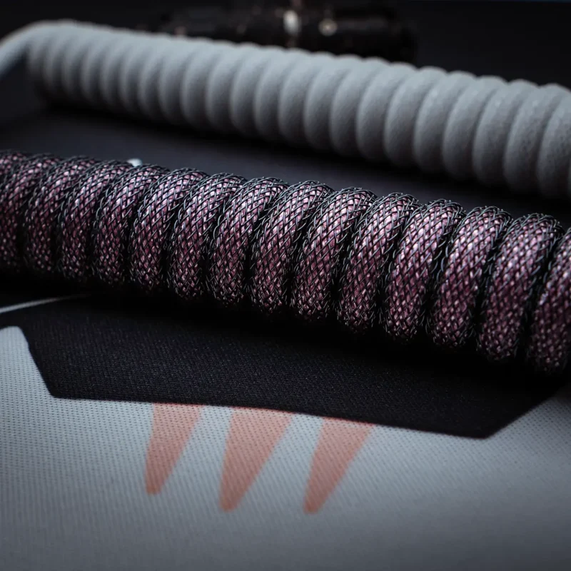 Aufgewickelte rosa schwarze Kabelnahaufnahme Textur Gewickelte schwarze und pinkfarbene Paracord-Tastaturkabel mit strukturierter Oberfläche. Zu den Merkmalen gehören abnehmbare Anschlüsse und eine langlebige Qualität, die sich ideal für kundenspezifische Setups eignet.
