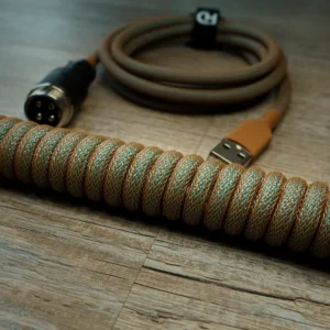 Coiled GMK Copper keyboard cable with a braided gold and green paracord finish, featuring a USB connector and CNC metal housing for durability.
