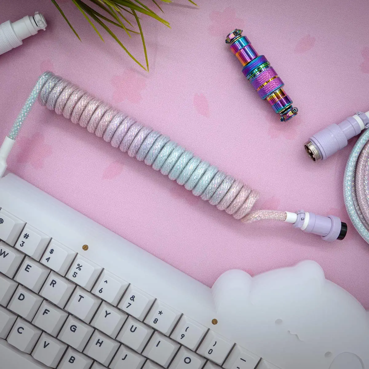 Cutie sparkle purple coiled cable The Cutie Sparkle Purple coiled cable with a pastel gradient sits on a pink deskmat featuring a cute bear design, next to a white keyboard. Also visible are an iridescent connector and part of an artificial plant.