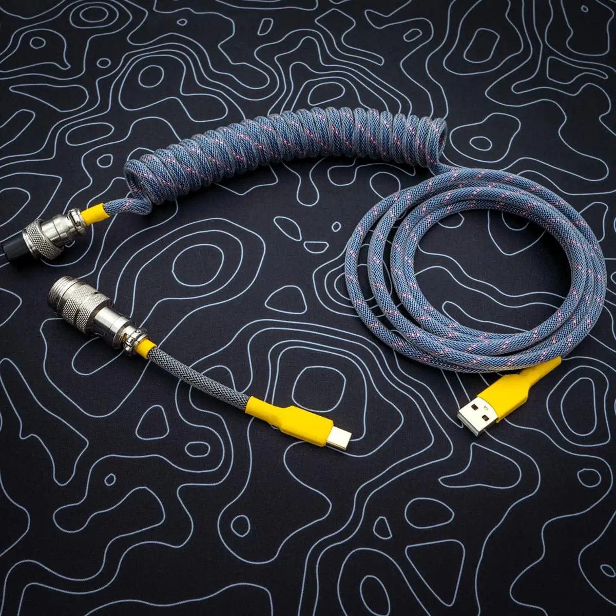 Dark blue coiled cable overhead aviator Coiled dark blue keyboard cable with yellow connectors, featuring USB-C and aviator plugs; quality paracord finish with smooth braiding for durability.