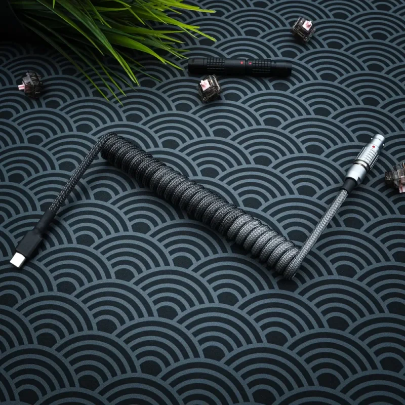Dark gray coiled keyboard cable featuring USB-C and aviator connectors, braided paracord finish, and sleek CNC metal housing for durability.