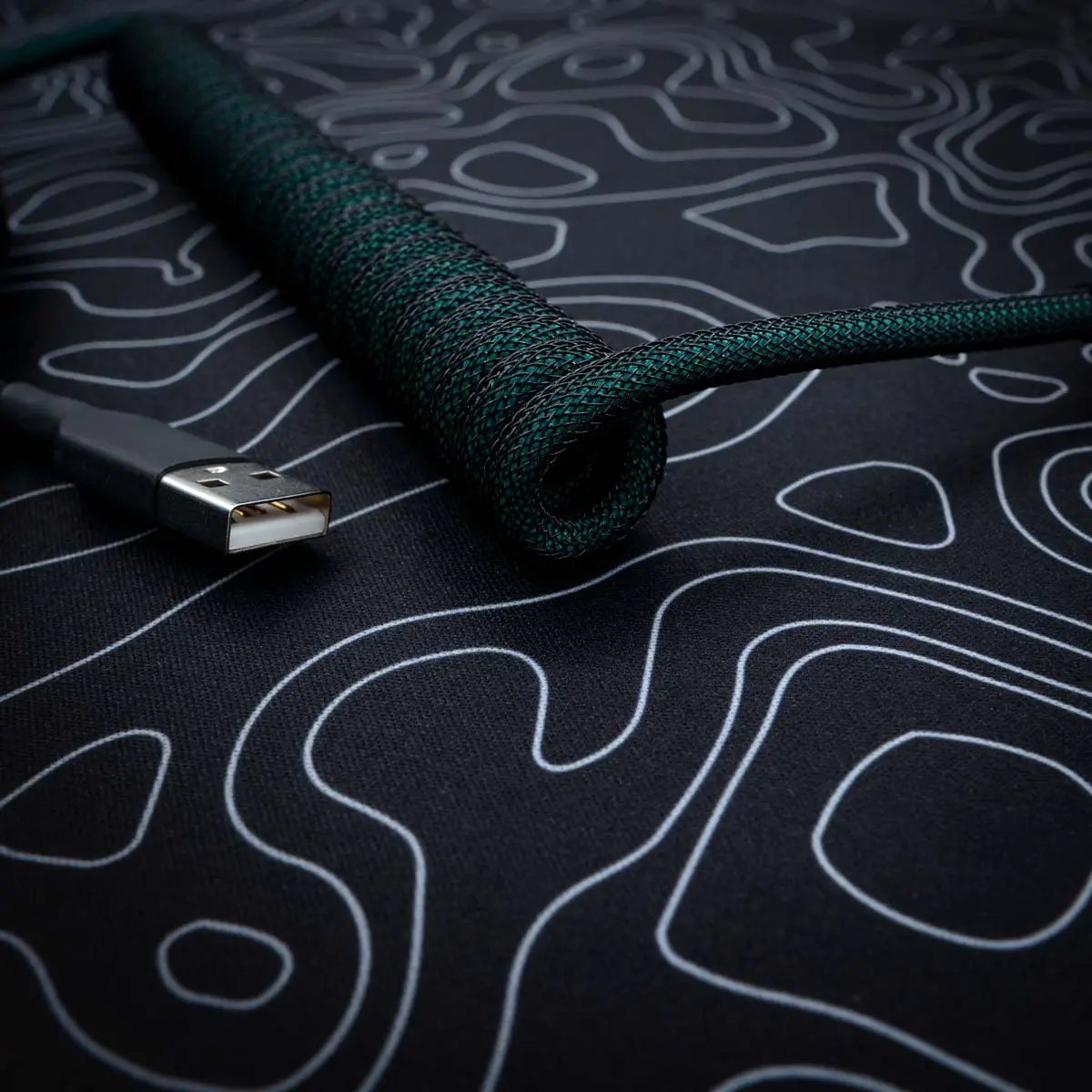 Dark green coiled usb cable angled view A stylish green coiled keyboard cable with a braided finish, featuring a USB connector, ideal for custom setups and high-quality connectivity.