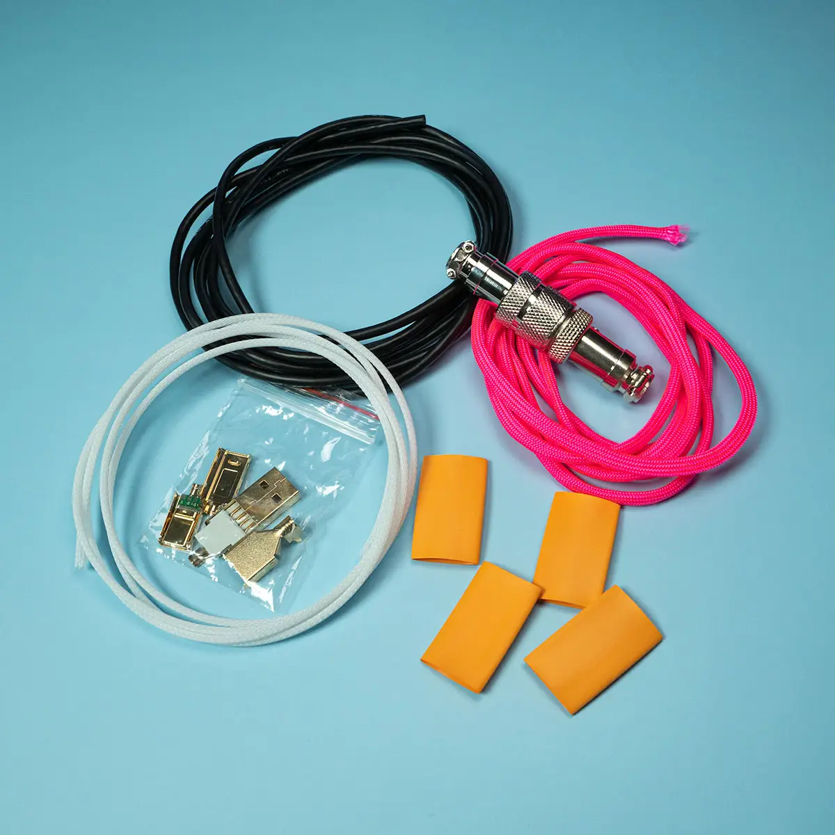 DIY USB Kit alle Teile Verschiedene elektronische Kabelkomponenten, darunter drei farbige Drähte, Anschlüsse in einer Plastiktüte und vier orangefarbene Schrumpfschläuche, sind als Teil eines DIY-USB-Kabelkits auf blauem Hintergrund angeordnet.