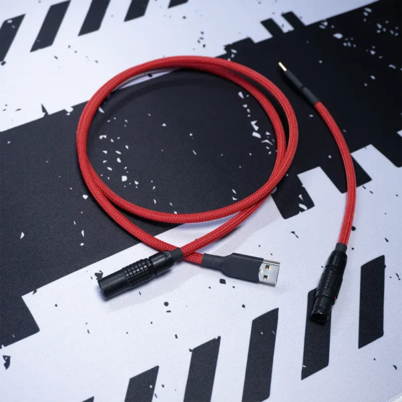 A Gmk Jamon red straight keyboard cable with a black Lemo connector rests on a black and white abstract patterned surface.