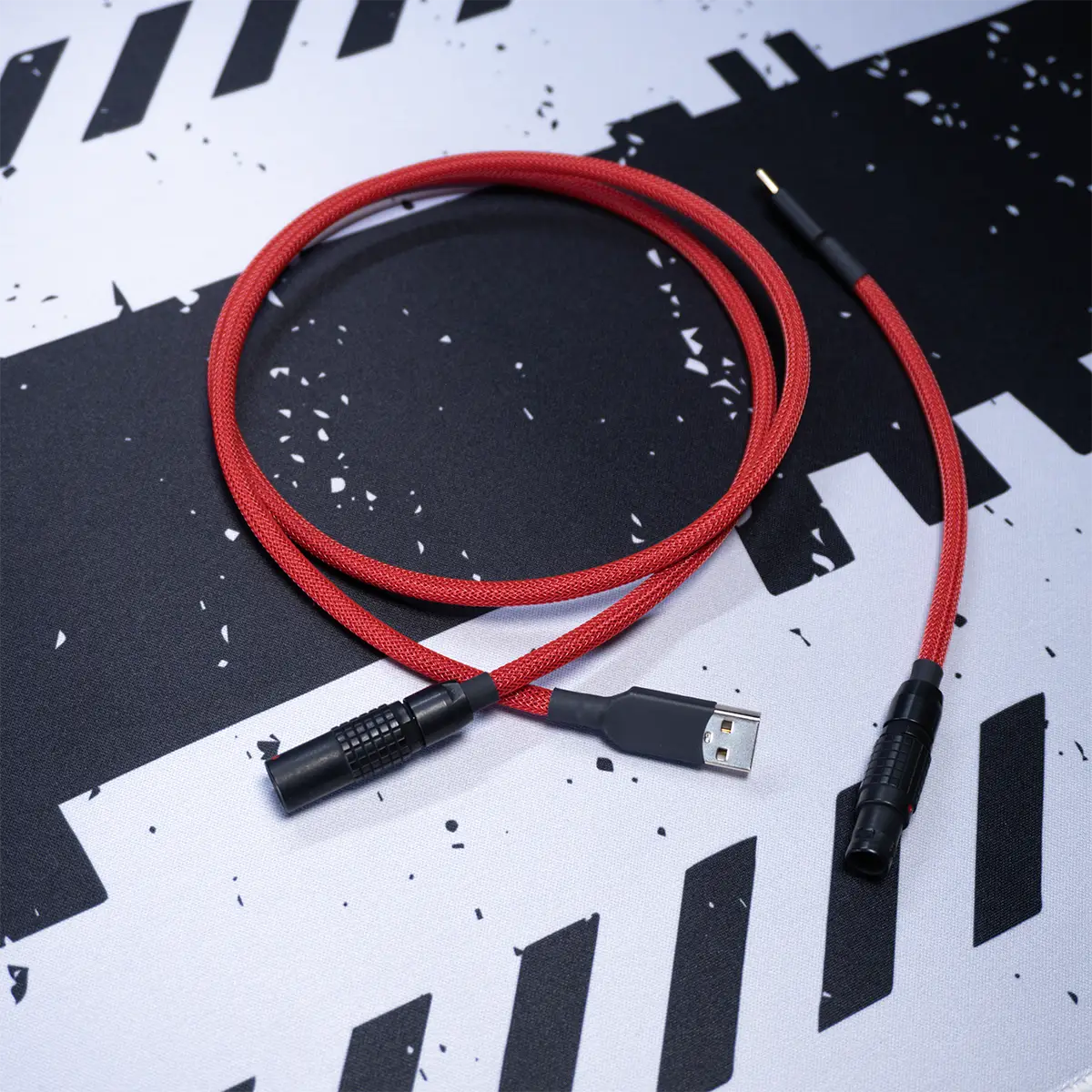 Gmk jamon red straight keyboard cable black lemo A Gmk Jamon red straight keyboard cable with a black Lemo connector rests on a black and white abstract patterned surface.