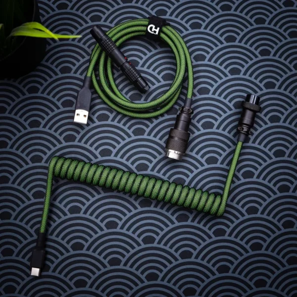 Custom green keyboard cable featuring a coiled design, USB-C and aviator connectors, durable paracord texture, and quality CNC metal housing.