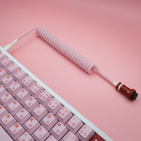 Pink coiled cable gx16 angled perspective A spiral pink keyboard cable with a soft-paracord finish, featuring a detachable aviator connector for flexible connections.