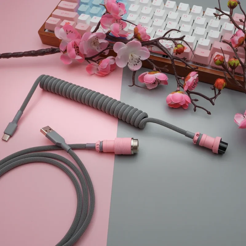 A coil-wrapped gray keyboard cable with USB-C and aviator connectors, featuring pink metal housing, quality braiding, and heatshrink detailing.