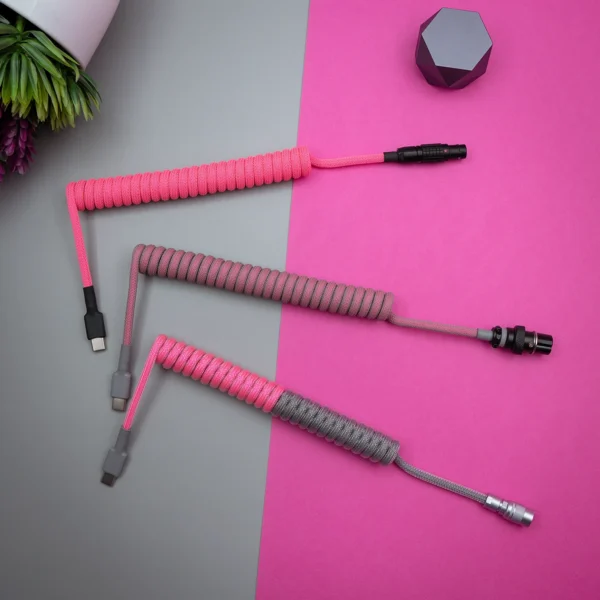 Three custom keyboard cables display vibrant pink and gray paracord braiding. Connectors include USB-C and aviator options, showcasing quality craftsmanship.
