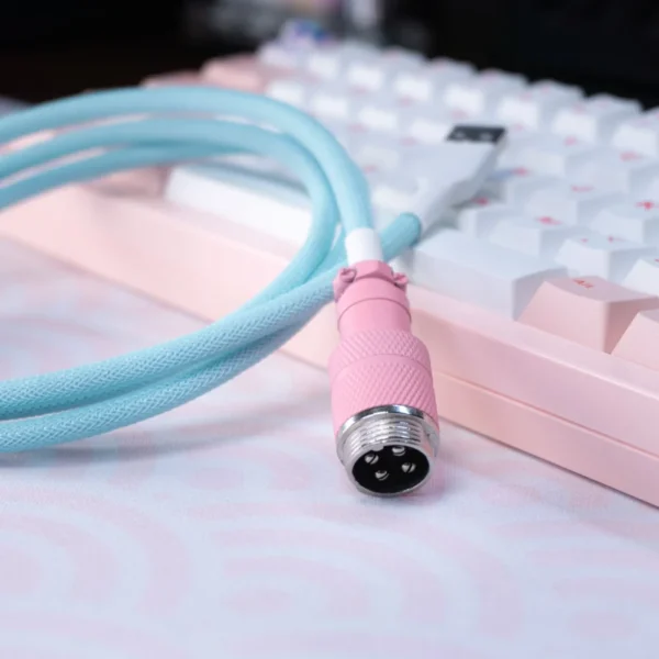 Coiled light blue keyboard cable with pink aviator connector and smooth braiding, showcasing quality craftsmanship and stylish design for custom setups.