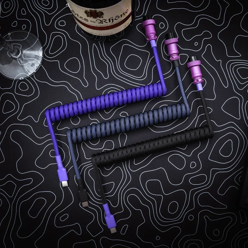 Purple black coiled cables top view aviator Three custom keyboard cables displayed on a textured background: one purple coiled