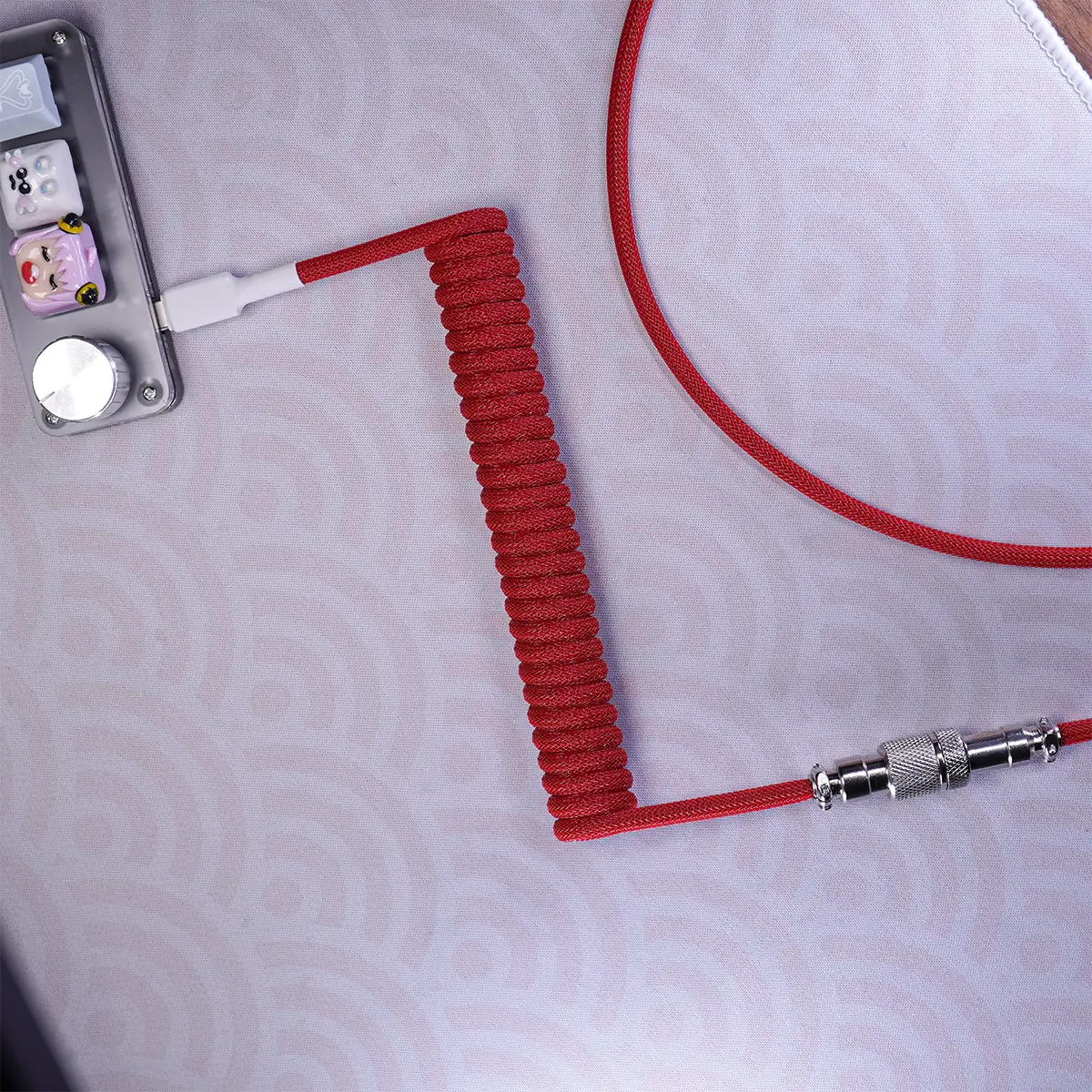 Red coiled cable with gx12 aviator A Red coiled cable with GX12 aviator is plugged into a mechanical keyboard with decorative keycaps, resting on a surface with a light gray patterned design.