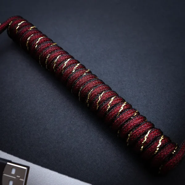 Red gold coiled cable angled view usb connector A stylish GMK Red Samurai Keyboard Cable featuring a coiled paracord design with gold accents, USB-C connector, and high-quality braiding for durability.