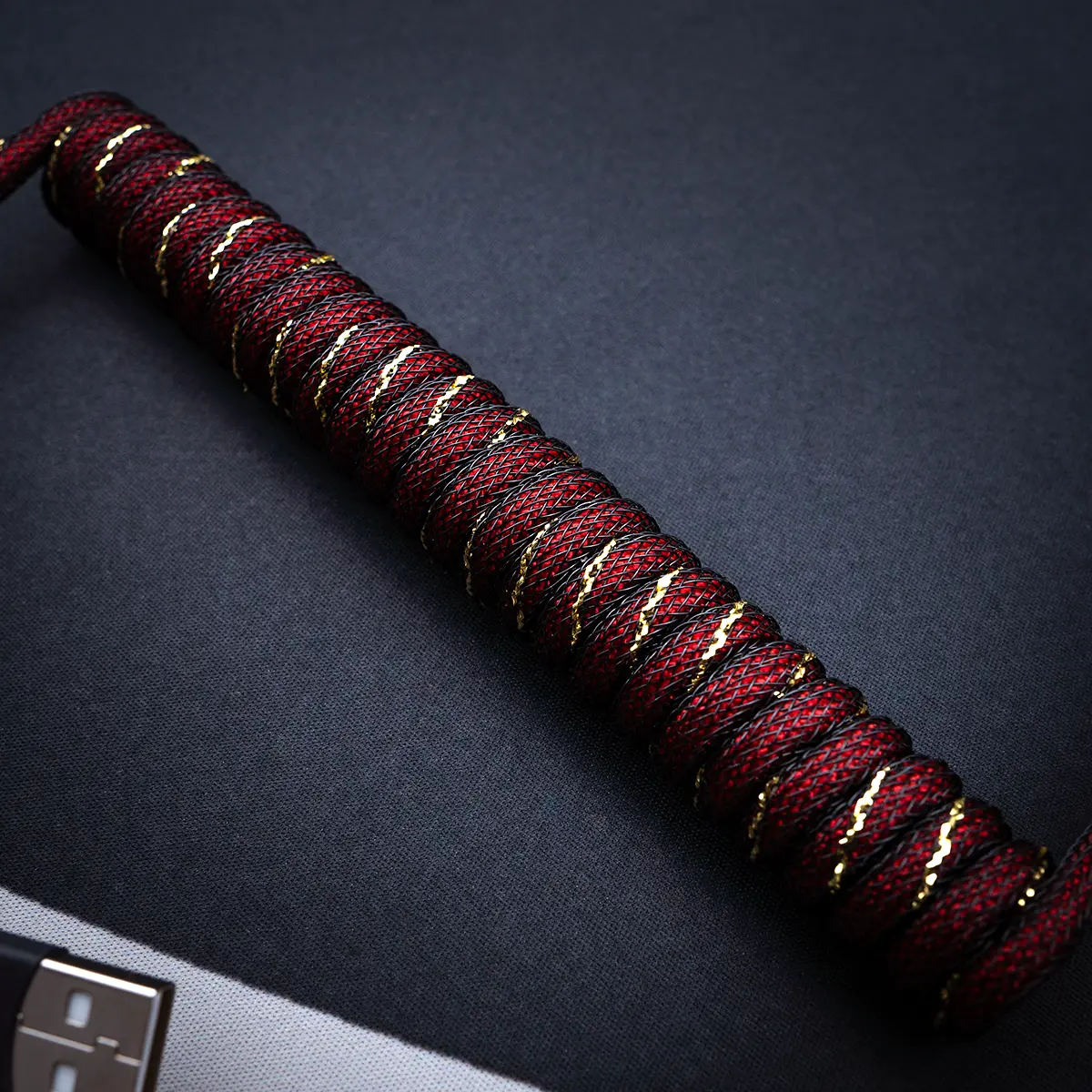 Rotgold Spiralkabel mit abgewinkelter Ansicht USB-Anschluss Ein stilvolles GMK Red Samurai Tastaturkabel mit einem gewickelten Paracord-Design mit goldenen Akzenten, USB-C-Anschluss und hochwertigem Geflecht für Langlebigkeit.