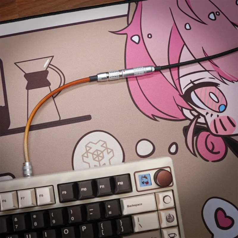 Eine mechanische Tastatur mit dunklen und hellen Tasten sitzt auf einer illustrierten Schreibtischunterlage mit einer rosahaarigen Anime-Figur; Verbunden wird es durch das Straight Keyboard Cable Nekoccino Theme, das quer über die Matte liegt.